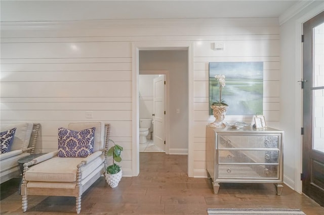 living area featuring wood walls, a healthy amount of sunlight, ornamental molding, and dark wood-type flooring