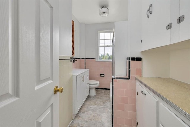 bathroom with vanity, toilet, tile walls, and a wainscoted wall