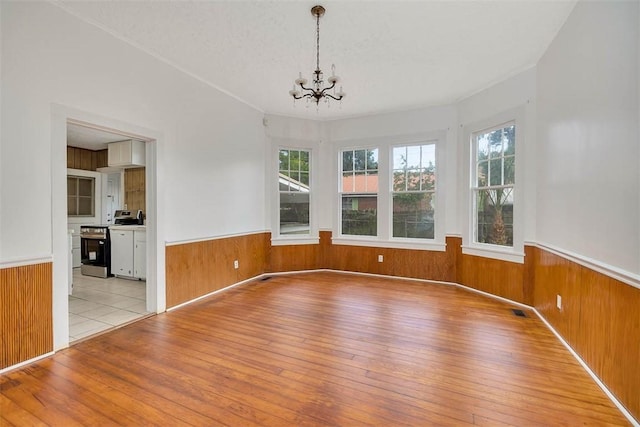 unfurnished dining area featuring wainscoting, wooden walls, light wood finished floors, a chandelier, and healthy amount of natural light