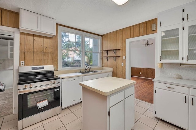 kitchen with stainless steel electric stove, white dishwasher, a sink, wooden walls, and light countertops