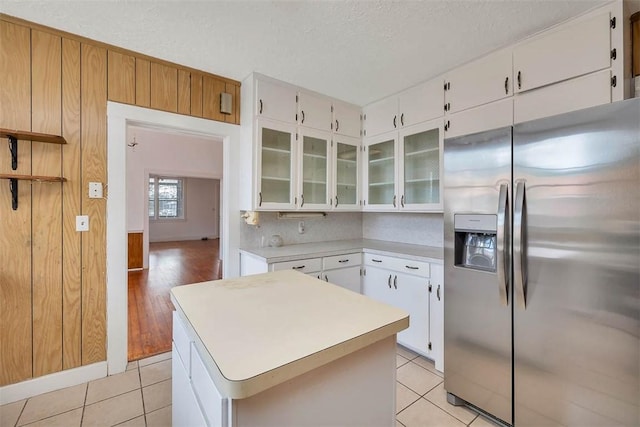 kitchen with stainless steel fridge with ice dispenser, light countertops, light tile patterned flooring, glass insert cabinets, and a textured ceiling