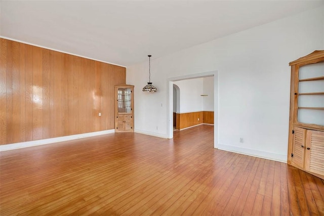 spare room featuring hardwood / wood-style flooring, arched walkways, baseboards, and wood walls