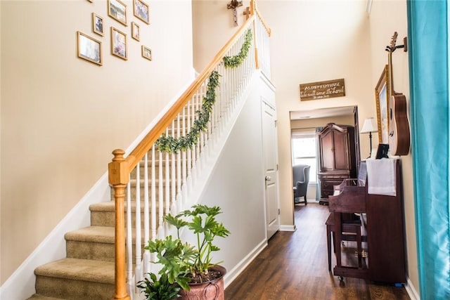 stairway featuring a high ceiling, baseboards, and wood finished floors