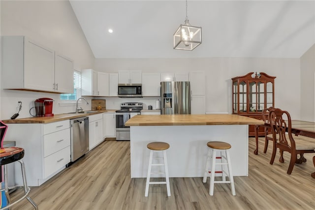 kitchen featuring wood counters, a center island, white cabinets, appliances with stainless steel finishes, and a breakfast bar area