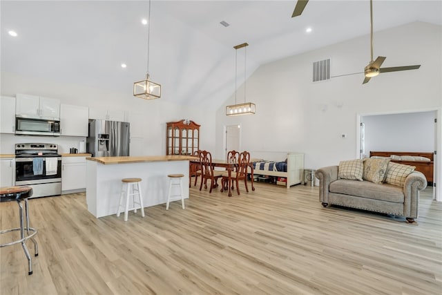 kitchen with high vaulted ceiling, white cabinets, a kitchen breakfast bar, light hardwood / wood-style flooring, and stainless steel appliances