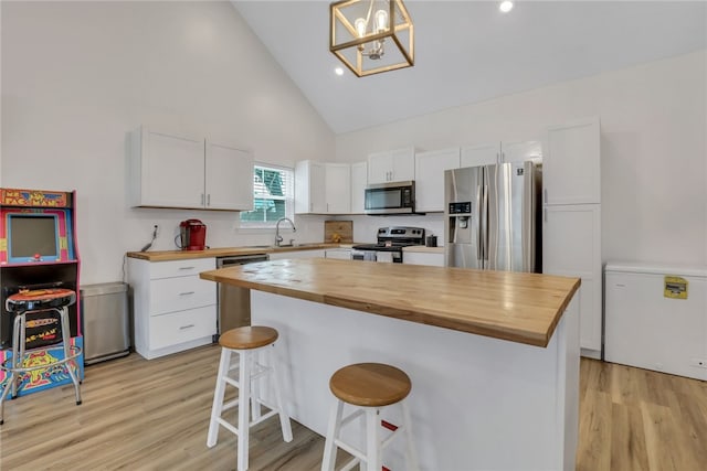 kitchen with appliances with stainless steel finishes, sink, decorative light fixtures, butcher block countertops, and white cabinetry