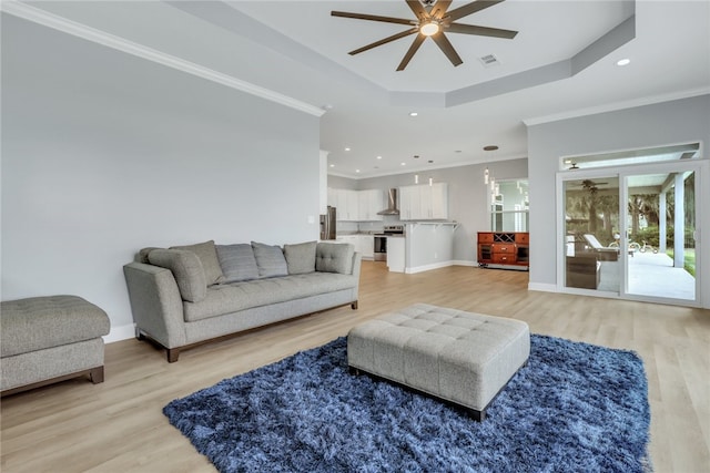 living room featuring ceiling fan, a raised ceiling, light wood-type flooring, and crown molding