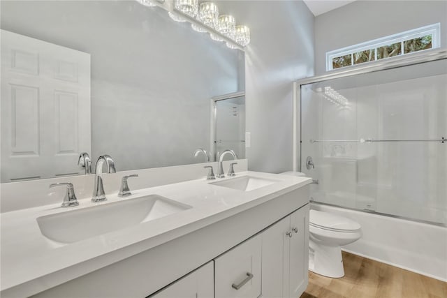 full bathroom featuring vanity, shower / bath combination with glass door, hardwood / wood-style flooring, toilet, and a notable chandelier