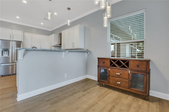 kitchen with ornamental molding, wall chimney exhaust hood, pendant lighting, stainless steel fridge with ice dispenser, and white cabinetry