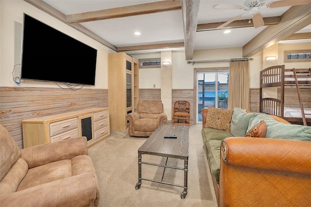 carpeted living room with ceiling fan, wooden walls, and beamed ceiling