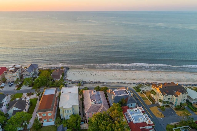 aerial view at dusk featuring a water view and a beach view