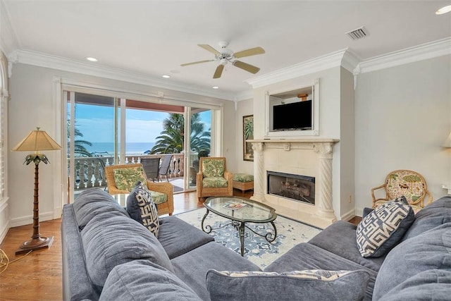 living room featuring crown molding, a fireplace, ceiling fan, and light wood-type flooring