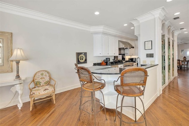 kitchen featuring wall chimney exhaust hood, kitchen peninsula, light hardwood / wood-style floors, and white cabinets