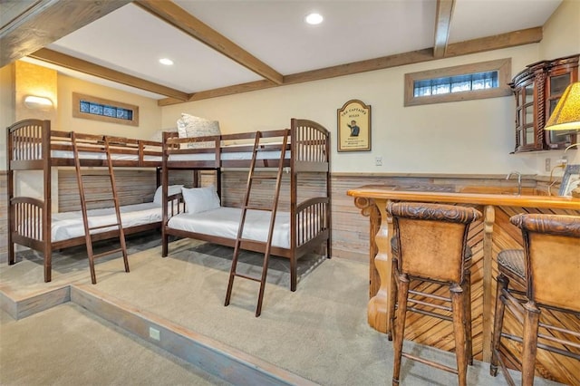 bedroom with light colored carpet, bar area, beam ceiling, and wood walls