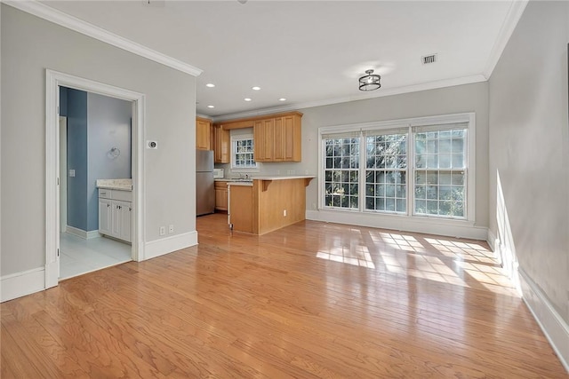 unfurnished living room featuring crown molding, sink, and light hardwood / wood-style floors