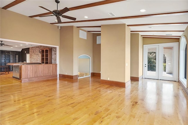 unfurnished living room featuring vaulted ceiling with beams, ceiling fan, french doors, and light wood-type flooring