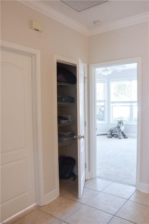 corridor with baseboards, ornamental molding, light tile patterned floors, and light carpet