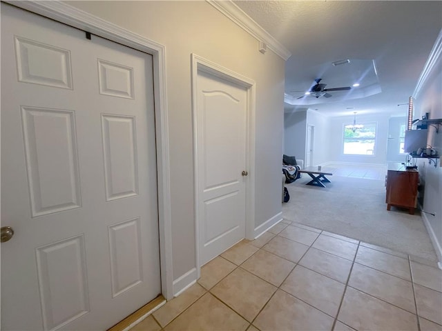 hall featuring crown molding, baseboards, light colored carpet, a textured ceiling, and light tile patterned floors