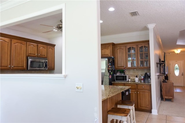kitchen with visible vents, stainless steel microwave, freestanding refrigerator, glass insert cabinets, and light tile patterned flooring