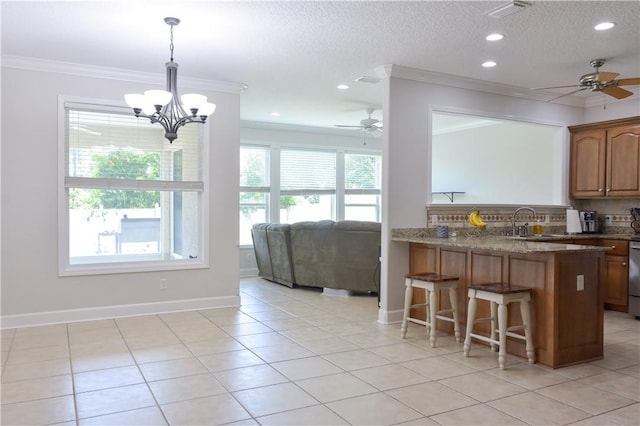 kitchen featuring a kitchen bar, a sink, ceiling fan with notable chandelier, a peninsula, and ornamental molding