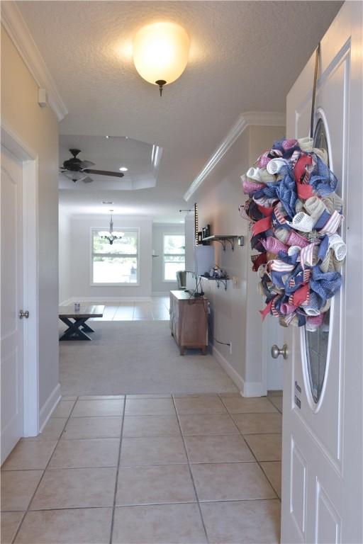 hall featuring light tile patterned flooring, a textured ceiling, ornamental molding, and baseboards