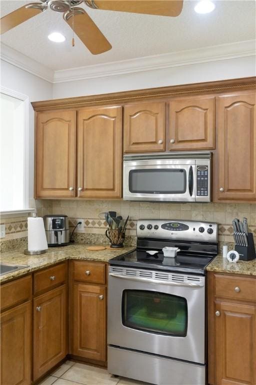 kitchen featuring light stone counters, a ceiling fan, appliances with stainless steel finishes, and ornamental molding