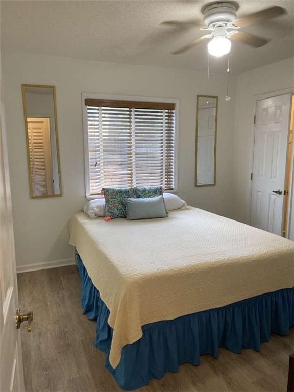 bedroom with a ceiling fan, a textured ceiling, baseboards, and wood finished floors