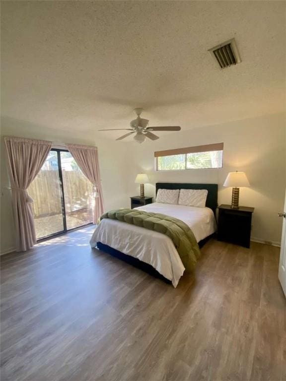 bedroom with a textured ceiling, visible vents, ceiling fan, wood finished floors, and access to exterior