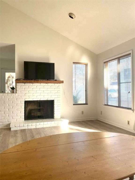 unfurnished living room with baseboards, lofted ceiling, a fireplace, and wood finished floors