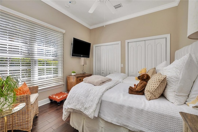 bedroom featuring wood finished floors, a ceiling fan, visible vents, two closets, and crown molding