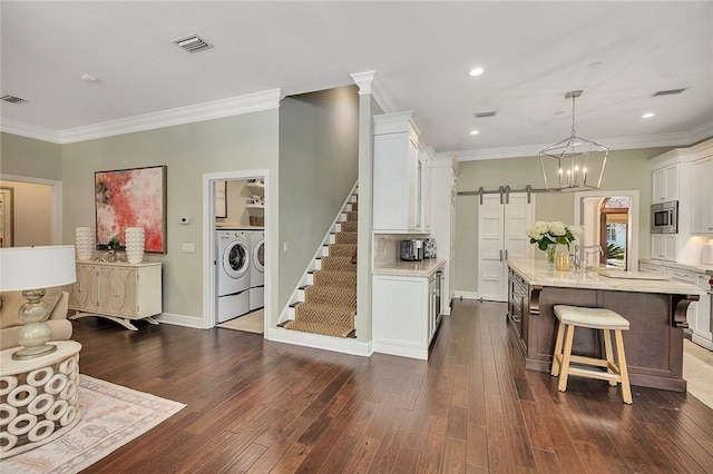 kitchen featuring a barn door, washing machine and dryer, visible vents, white cabinetry, and stainless steel microwave