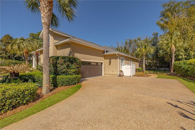 view of property exterior featuring a garage, concrete driveway, fence, and stucco siding