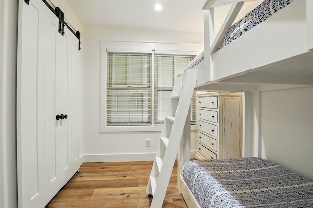 bedroom with baseboards, a barn door, light wood-style flooring, and recessed lighting
