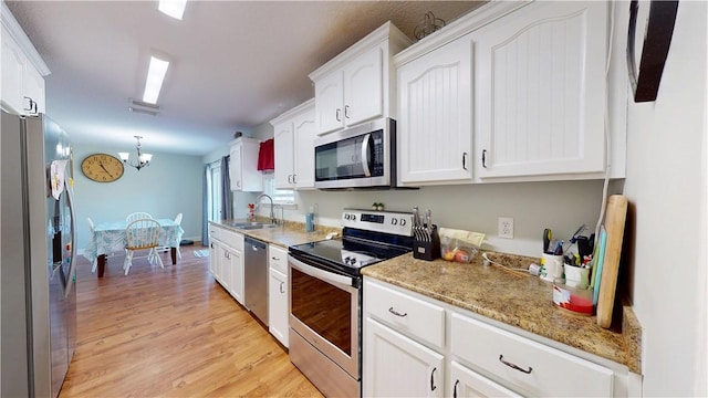 kitchen with a sink, light wood-style floors, appliances with stainless steel finishes, white cabinets, and an inviting chandelier