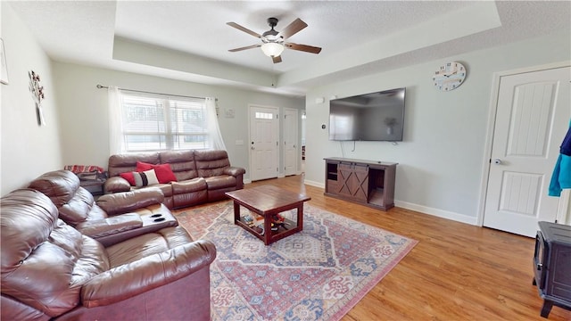 living area featuring a tray ceiling, baseboards, a ceiling fan, and light wood finished floors