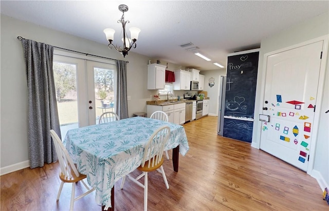 dining space with baseboards, a chandelier, light wood-style flooring, french doors, and a textured ceiling