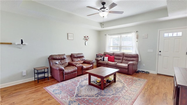 living room featuring a raised ceiling, baseboards, light wood-type flooring, and ceiling fan