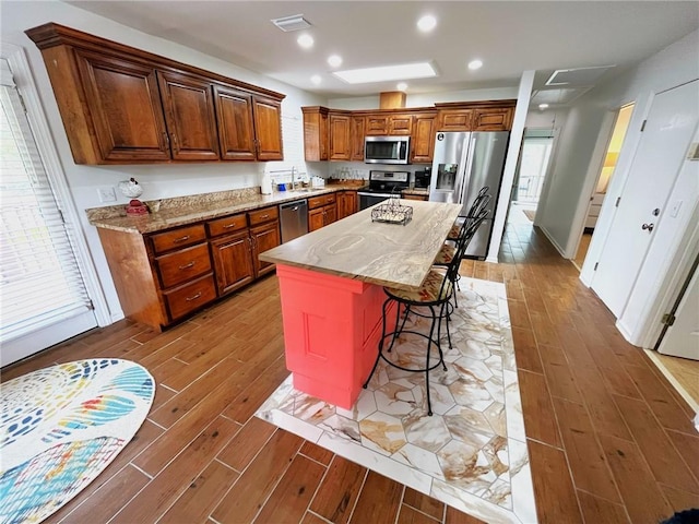 kitchen featuring hardwood / wood-style floors, a breakfast bar, appliances with stainless steel finishes, a kitchen island, and light stone counters