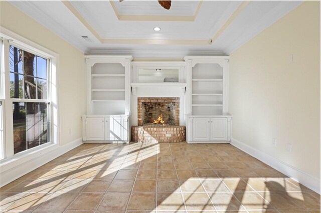 unfurnished living room featuring a brick fireplace, ornamental molding, a raised ceiling, ceiling fan, and built in features