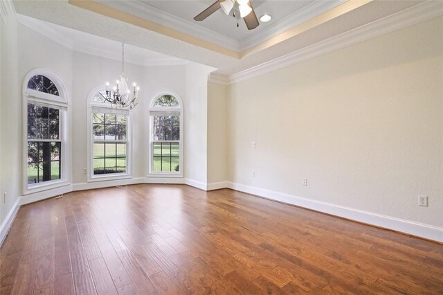 empty room with ceiling fan with notable chandelier, a raised ceiling, ornamental molding, and dark wood-type flooring