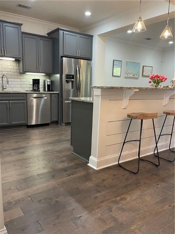 803 Mariners Cir, Saint Simons Island, GA 31522 - kitchen with appliances with stainless steel finishes, ornamental molding, a kitchen bar, light stone countertops, and dark wood-type flooring