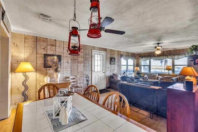 tiled dining room featuring wood walls and ceiling fan