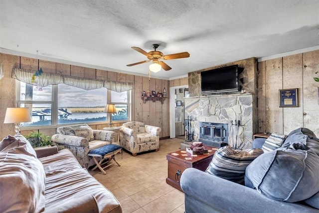 living room with a textured ceiling, ceiling fan, wooden walls, light tile patterned floors, and a fireplace