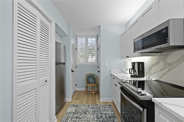 kitchen featuring appliances with stainless steel finishes, light wood finished floors, light stone countertops, baseboards, and white cabinetry