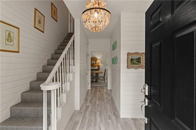 entrance foyer featuring wooden walls, light hardwood / wood-style floors, and a notable chandelier