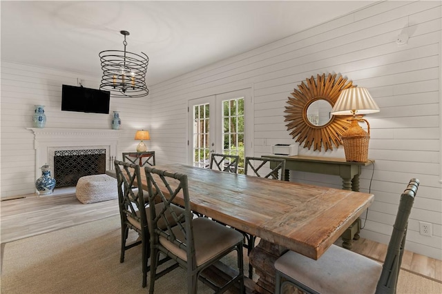 dining area with french doors, an inviting chandelier, light hardwood / wood-style flooring, and wooden walls