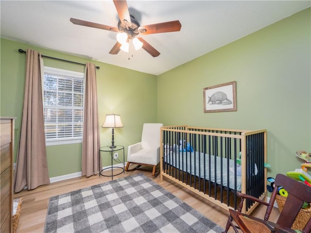 bedroom featuring ceiling fan, light hardwood / wood-style floors, and a crib