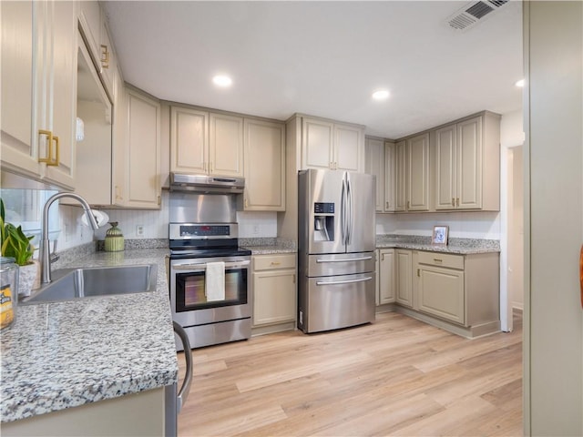 kitchen with appliances with stainless steel finishes, sink, light stone counters, and light hardwood / wood-style flooring