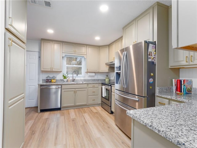 kitchen featuring sink, light stone counters, appliances with stainless steel finishes, light hardwood / wood-style floors, and cream cabinetry