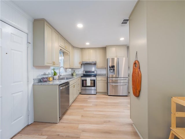 kitchen with sink, crown molding, appliances with stainless steel finishes, light stone countertops, and light wood-type flooring